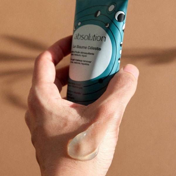 Iemand houdt de tube van Absolution  Le Baume Céleste vast met de textuur op de hand