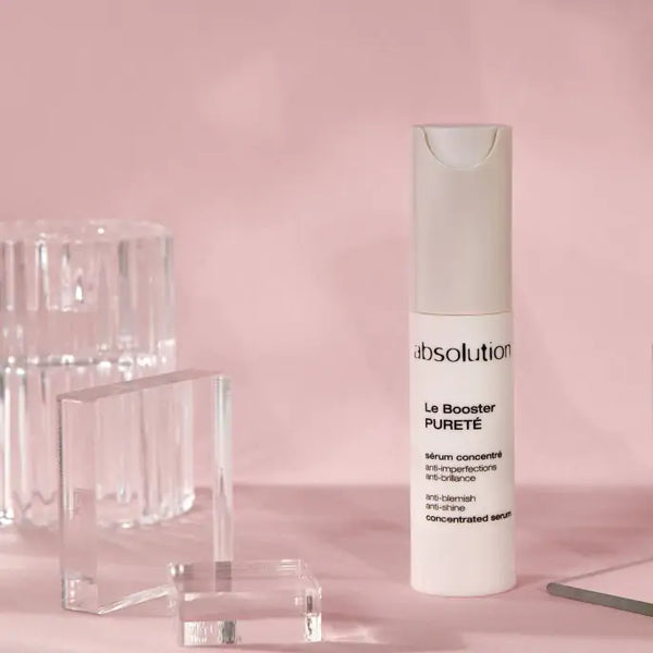 Absolution Le Booster Pureté serum op een pastelroze achtergrond met glazen blokken ernaast