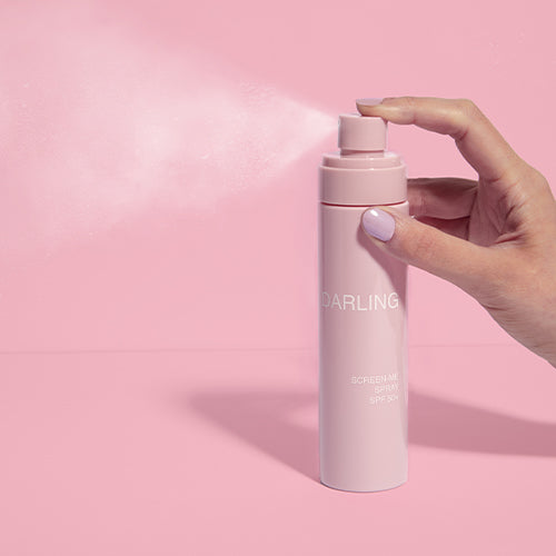 Hand sprayt Darling Screen-Me SPF 50 zonnebrandlotion in de lucht