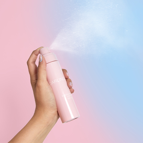 Persoon die Darling Screen-Me Spray SPF 30 in de lucht sprayt voor gebruik