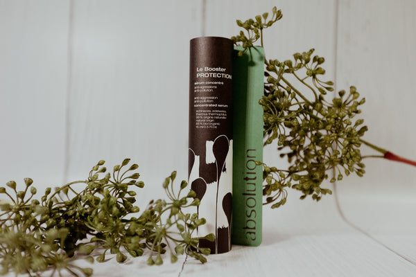 Absolution Le Booster Protection serum tussen groene planten, voor een frisse, natuurlijke uitstraling.