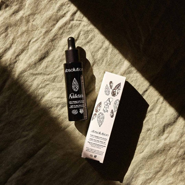 Addiction, l’Huile Visage en verpakking liggen op een ongestreken doek, met zachte schaduw voor een elegante uitstraling