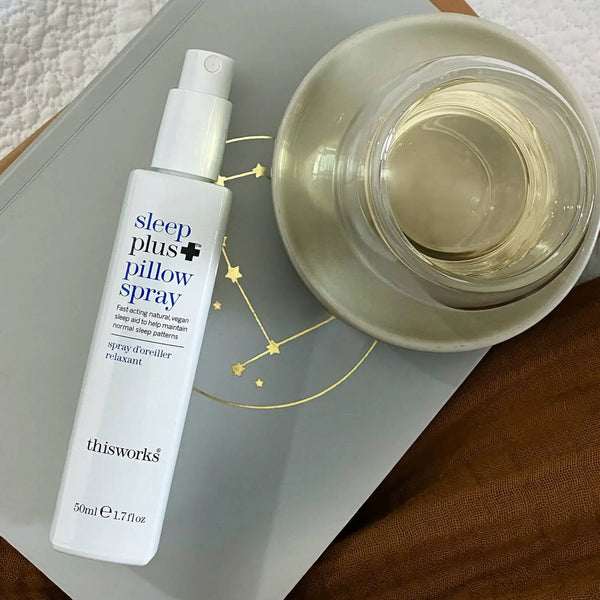 Sfeerbeeld van This Works Sleep Plus+ Pillow Spray 50 ml op een boek met een glas thee