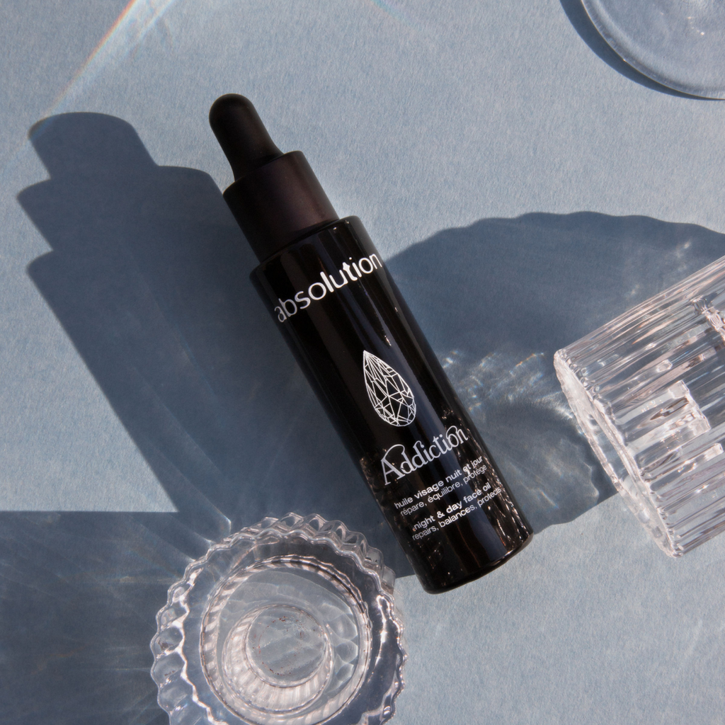 Flesje van Addiction, l’Huile Visage ligt met een glasachtige schaduw, wat de luxe uitstraling benadrukt.