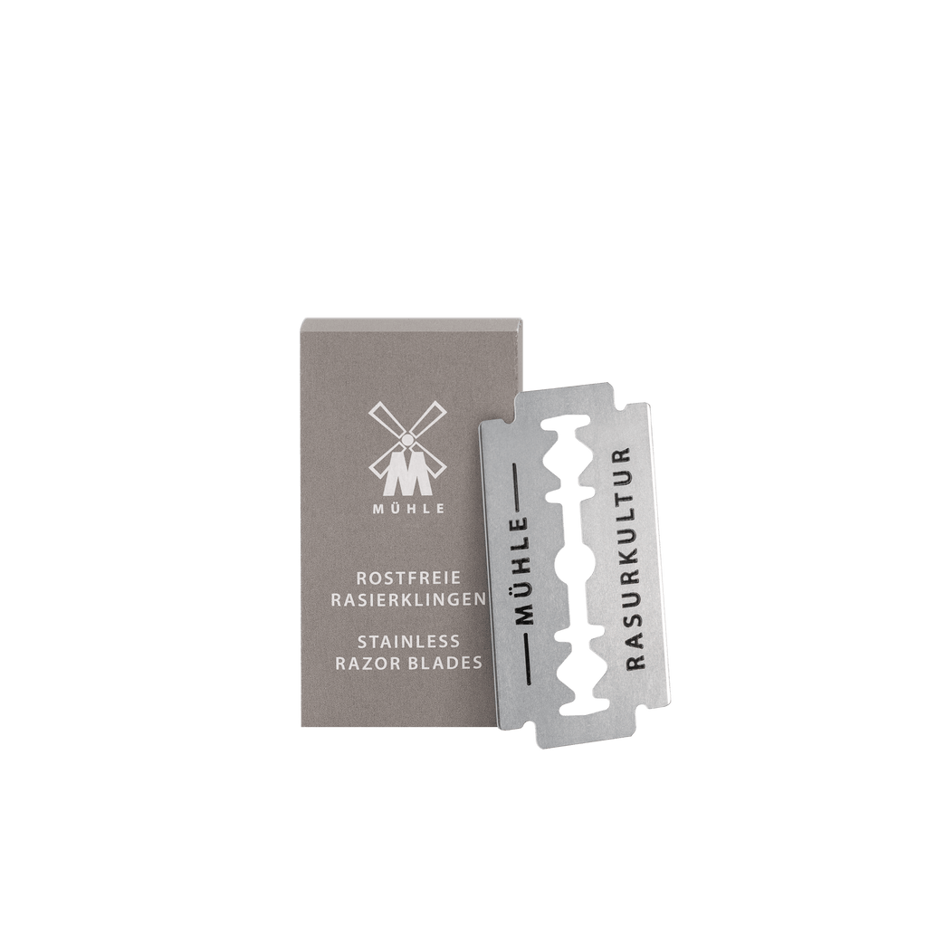 Verpakking en losse Mühle roestvrijstalen scheermesje op een geruit oppervlak, met opschrift 'Rostfreie Rasierklingen' en 'Stainless Razor Blades