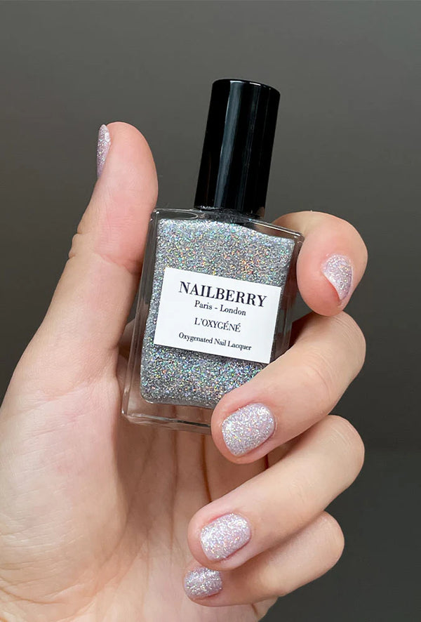Model met Cosmic Top Coat-glitternagels, houdt een Nailberry flesje vast
